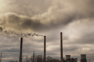 Factory smokestacks emitting pollution into cloudy sky, highlighting environmental toxins