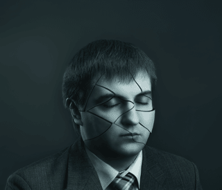 Man in suit with closed eyes, face showing cracked glass effect, symbolizing brain fog and fatigue