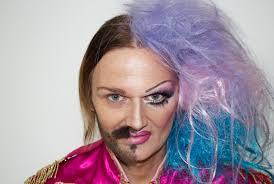 Person with half face styled masculine with beard and other half feminine with makeup and colorful wig, symbolizing hormone balance and gender expression.