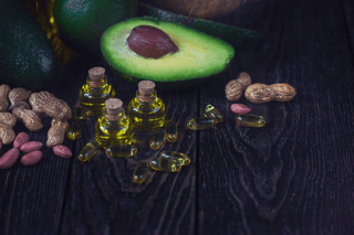 Avocado, peanuts, oil capsules, and bottles of oil on dark wood, healthy fats concept