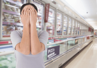 Person in a grocery store frozen food aisle covering face, illustrating food sensitivity stress